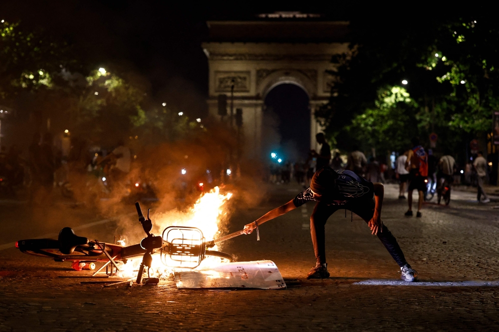 A member of the public holds an object to a burning bicycle on the Avenue de la Grande Armee during gatherings after PSG won the UEFA Champions League final between Paris Saint-Germain (PSG) and Arsenal FC played in Budapest (Photo by Kenzo Tribouillard / AFP)