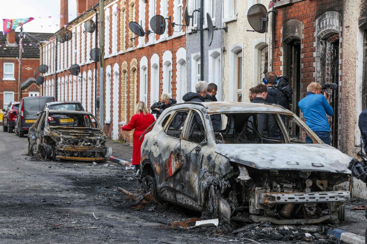 Residents and members of the media look at burnt-out cars and homes after demonstrations turned violent the night before, in eastern Belfast, Northern Ireland, on June 10, 2026. Photo by Paul Faith / AFP