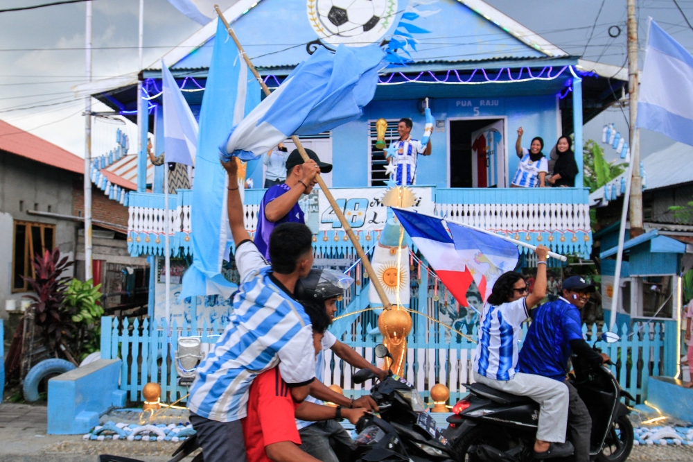 Argentina fan and fisherman Muhammad Yusuf (back C) holds a replica of the World Cup trophy as football fans pass his house, painted in the colours of the Argentine national team in Indonesia's West Sulawesi on June 11, 2026. (Photo by Muhammad Salim / AFP)