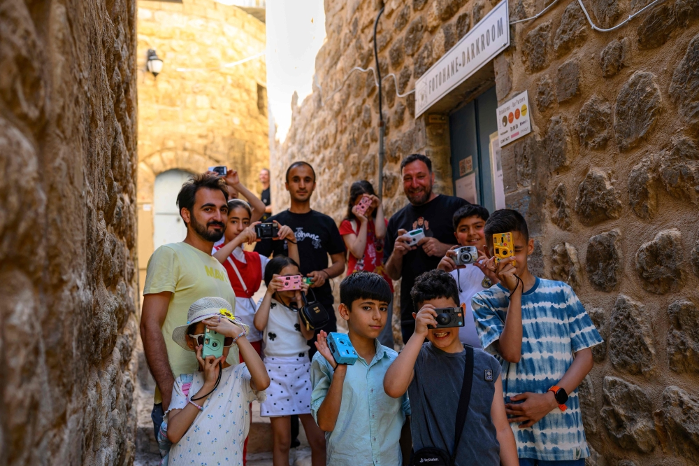 A group of children pose with their educators as they take pictures in the streets with film cameras during a workshop on June 14, 2026. (Photo by Yasin Akgul / AFP)