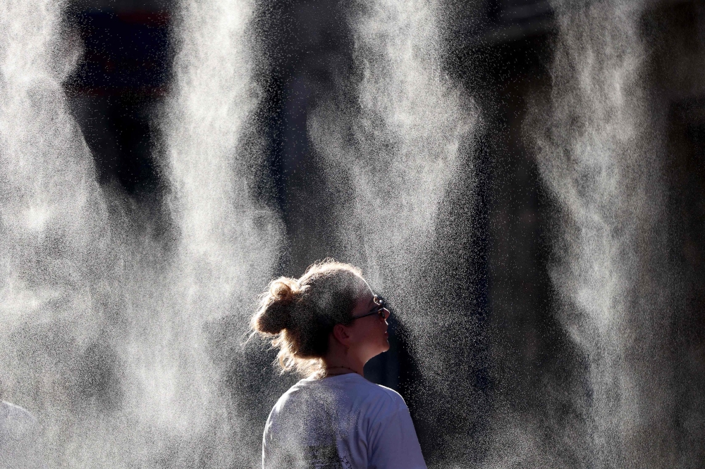 A woman cools off under a mist sprayer during the annual street music festival 'Fete de la Musique' while taking part in a heatwave in Bordeaux, southwestern France on June 21, 2026. (Photo by ROMAIN PERROCHEAU / AFP)
