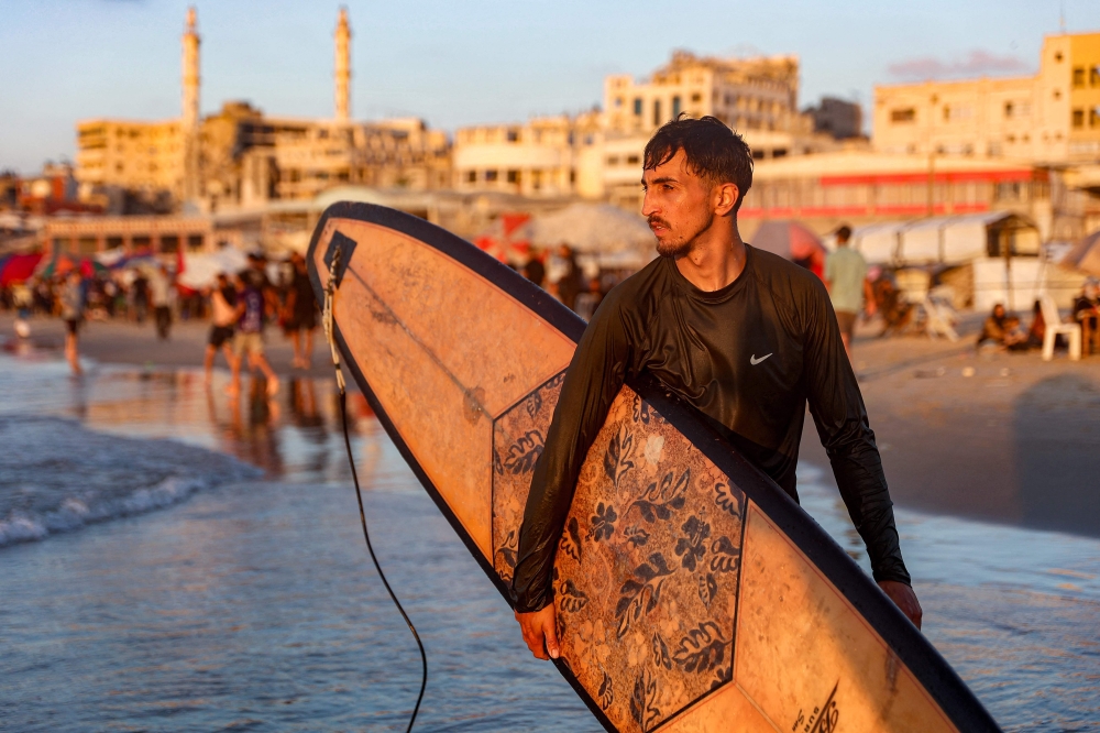 Palestinian surfer Tahseen Abu Assi, 23, takes his surfboard out into the Mediterranean sea off a beach in Gaza City on June 21, 2026. (Photo by Omar Al-Qattaa / AFP)