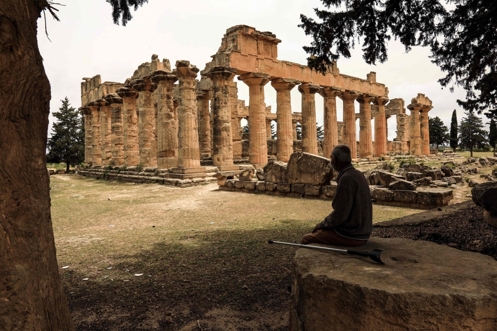 (Files) A man sits in the shade in front of the Temple of Zeus at the archaeological site of Cyrene, near the town of Shahat on Libya's northeastern Mediterranean coast, on May 18, 2026. (Photo by Abdullah Doma / AFP)