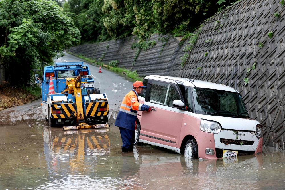 A tow lorry driver retrieves a partially submerged car after flooding in the town of Kashiwara, Osaka prefecture on June 26, 2026.  (Photo by Paul Miller/ AFP)
