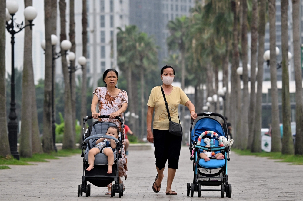 This photo taken on June 29, 2026, shows women pushing strollers with children along a sidewalk in Hanoi. Photo by Nhac Nguyen / AFP
