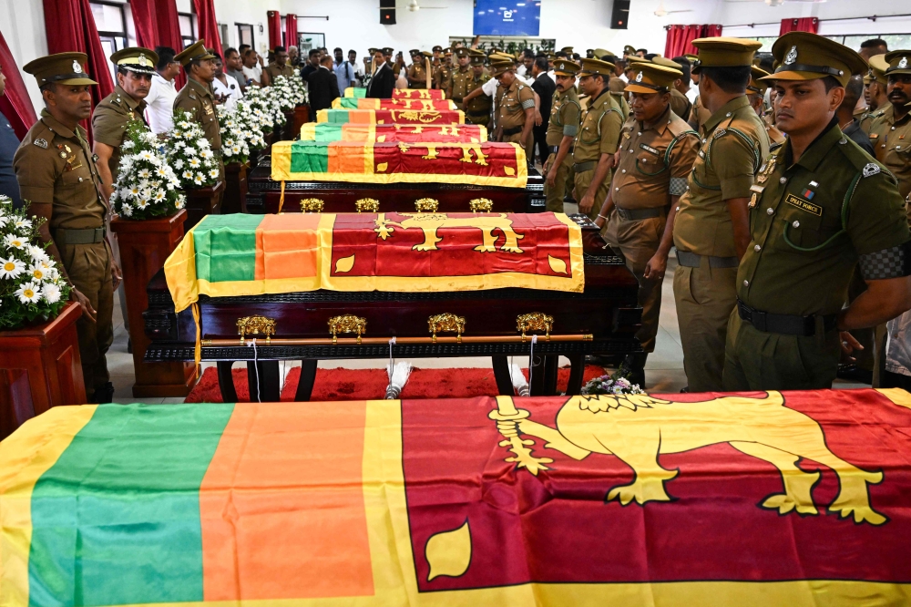 Security personnel pay tribute as they stand next to coffins of seven guards killed during Negombo prison riot in Colombo July 8, 2026. (Photo by Ishara S. Kodikara / AFP)