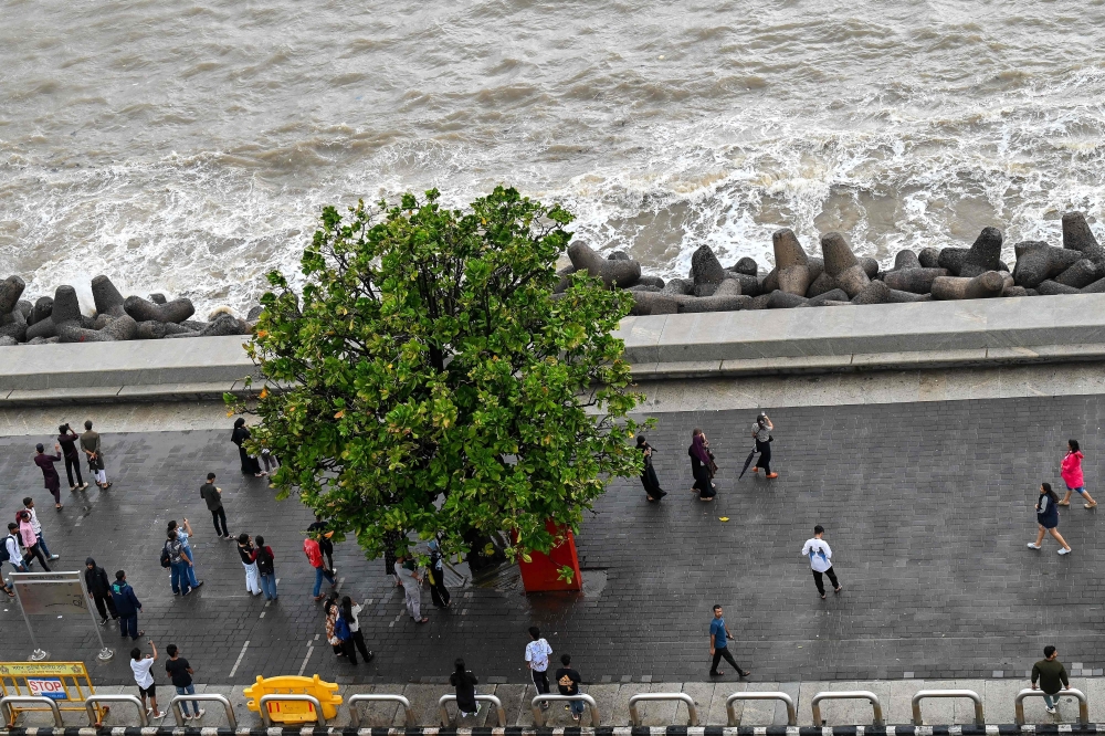 This photograph taken on July 7, 2026 shows pedestrians walking on the footpath along the seafront in Mumbai. (Photo by Punit Paranjpe / AFP)