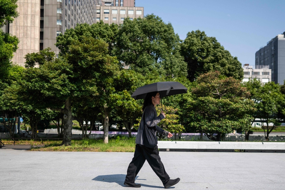 A man wearing all black walks through a park with an umbrella in Tokyo on July 22, 2026. (Photo by Andrew Caballero-Reynolds / AFP)