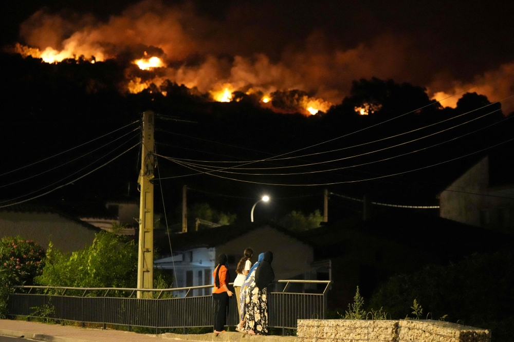 Residents watch the flames on hill crests as firefighters battle a wildfire in Cebreros area, near Avila, 80 kms west of Madrid at night on July 24, 2026. (Photo by Cesar MANSO / AFP)