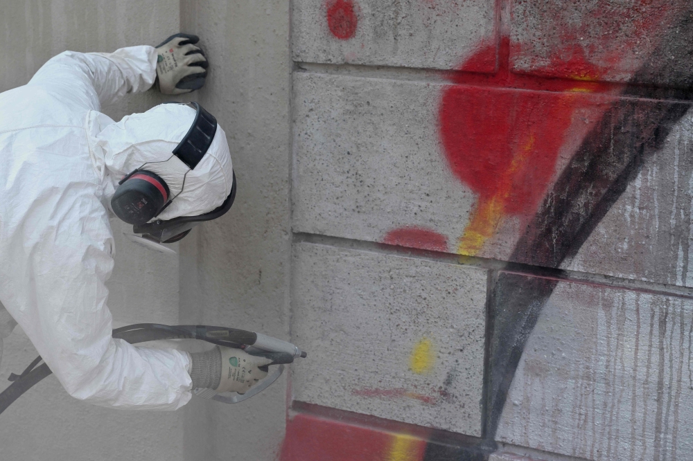 Valerio Tuveri works to erase graffiti from one of the external walls of Villa Sciarra in Rome on July 27, 2026. (Photo by Alberto Pizzoli / AFP)