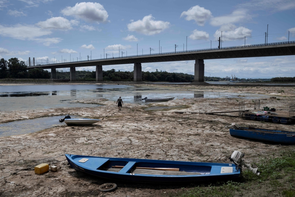 A fisherman tries to move his boat, blocked by algae on the bottom of the Danube river in front of the Calafat-Vidin bridge, connecting Bulgaria and Romania near the village Antimovo, southeastern Bulgaria, on July 22, 2026. (Photo by Nikolay DOYCHINOV / AFP)
