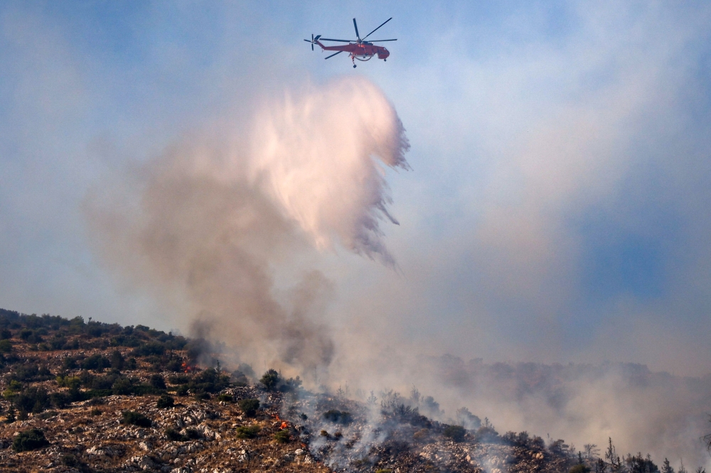 A firefighting helicopter drops water on a wildfire in Haidari, a suburb west of Athens, on July 31, 2026. (Photo by Aris Oikonomou / AFP)