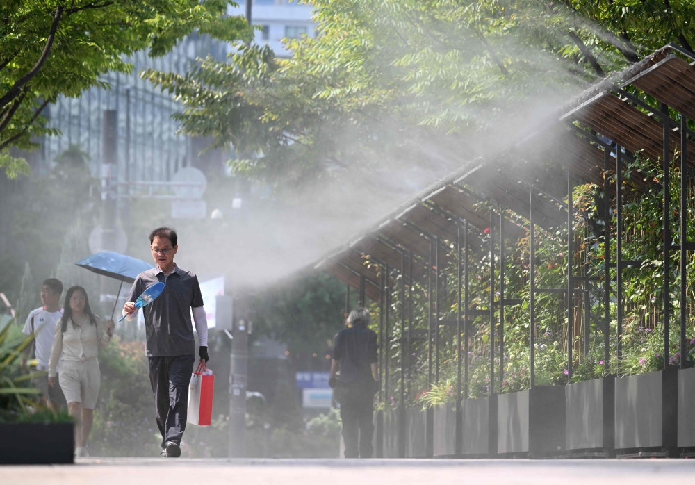 Pedestrians walk along a mist-spraying zone to cool off on a street in Seoul on August 3, 2026, as a scorching heat wave continues to grip South Korea. (Photo by Jung Yeon-je / AFP)