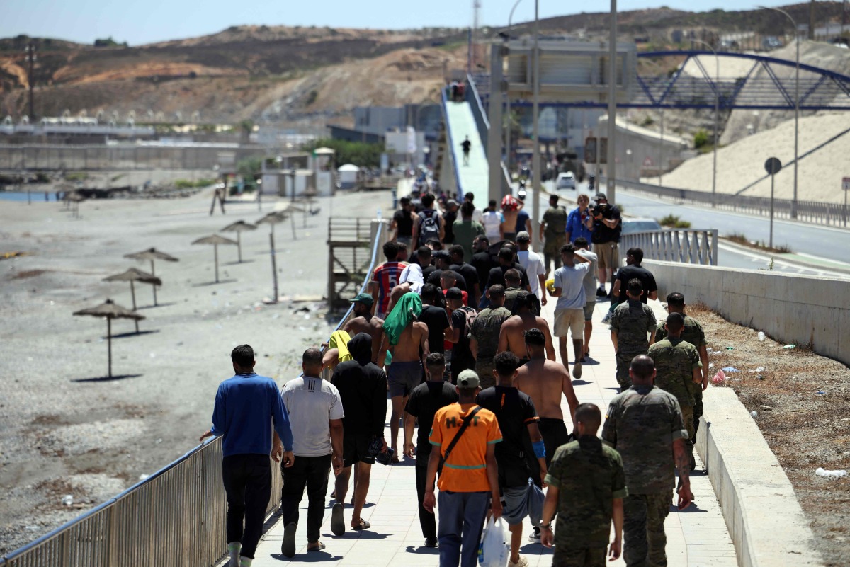 A group of migrants approach the border post to make their way back to Morocco, escorted by Spanish infantry soldiers, in the Spain's north African enclave of Ceuta, on August 2, 2026. Photo by Henry NICHOLLS / AFP
