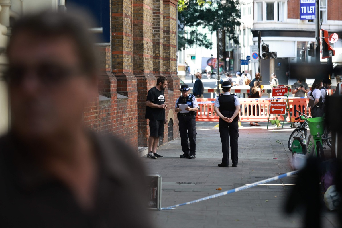 Police community support officers (PCSOs) speak to a person near cordon tape at Endell road in covent garden, central London on August 5, 2026. Photo by Henry NICHOLLS / AFP