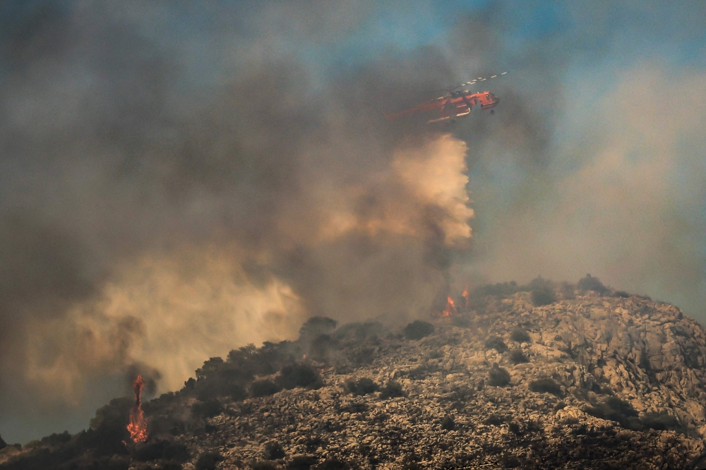 A firefighting helicopter drops water during a wildfire in the island of Salamina, near Athens, on August 16, 2026. (Photo by Yannis Panagopoulos / Eurokinissi / AFP)