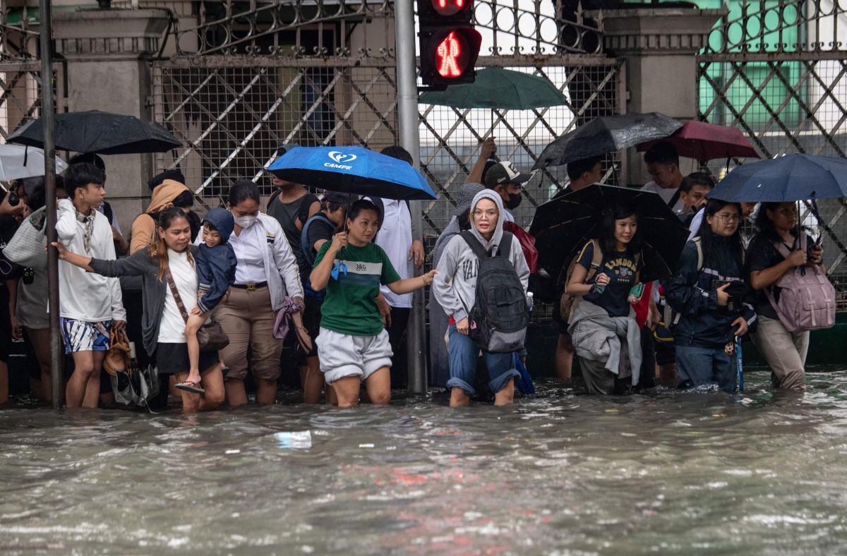 Commuters wade through a flooded street triggered by heavy monsoon rains in Manila on August 17, 2026. (Photo by Ted ALJIBE / AFP)
