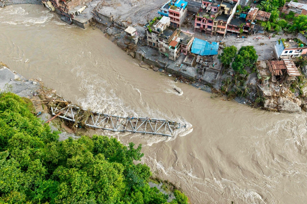 An aerial view shows a collapsed bridge along with houses lying deluged in sludge after flash floods at Devighat, Bidur Municipality in nepal's Nuwakot district on August 27, 2026.  (Photo by Prabin RANABHAT / AFP)