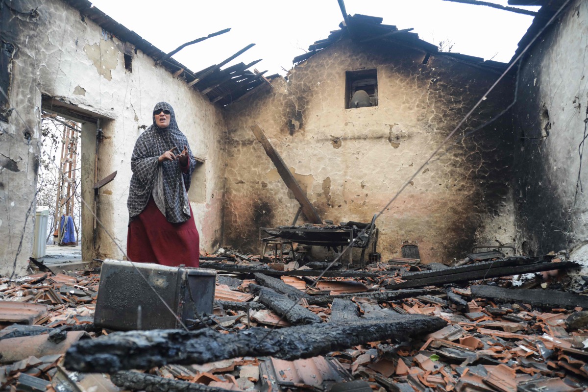 A woman inspects her damaged house after it was burned down in a forest fire in Bordj T'har, a town and commune in Algeria's northeastern Jijel Province, on August 27, 2026. (Photo by AFP)