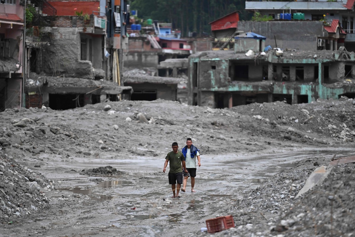 Flash flood survivors walk through sludge past damaged houses searching for salvageable belongings at Trishuli Center in Nepal's Nuwakot district on August 30, 2026. Photo by Arun SANKAR / AFP