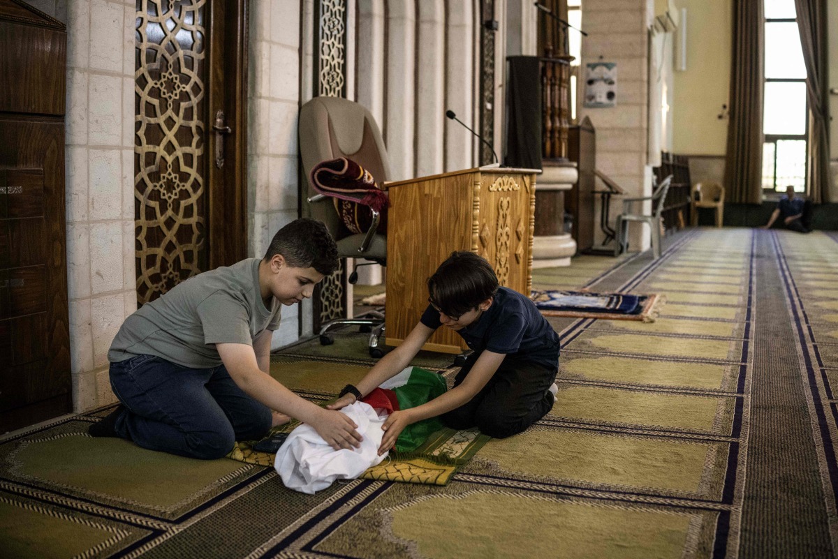 This photo taken on June 6, 2026 shows Kinan Abou Haikal (L), the elder brother of seven-month-old baby Sam Fahd Abou Haikal, sitting next to his body at the Abou Heisheh Mosque in Hebron, in the Israeli-occupied West Bank. (Photo by JOHN WESSELS / AFP)