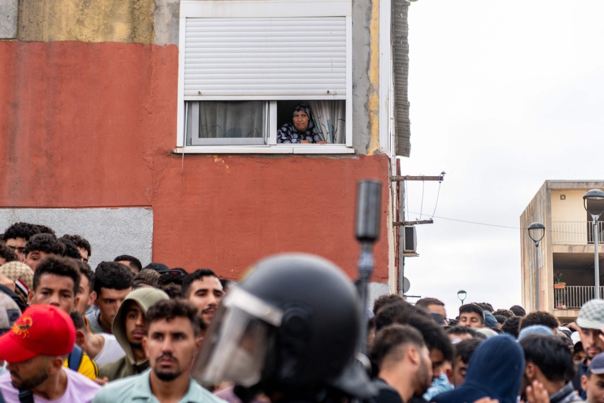 A resident watches from her window migrants waiting on the sidewalk before being registered in Loma Colmenar district of Ceuta on August 31, 2026. Photo by Antonio Sempere / AFP