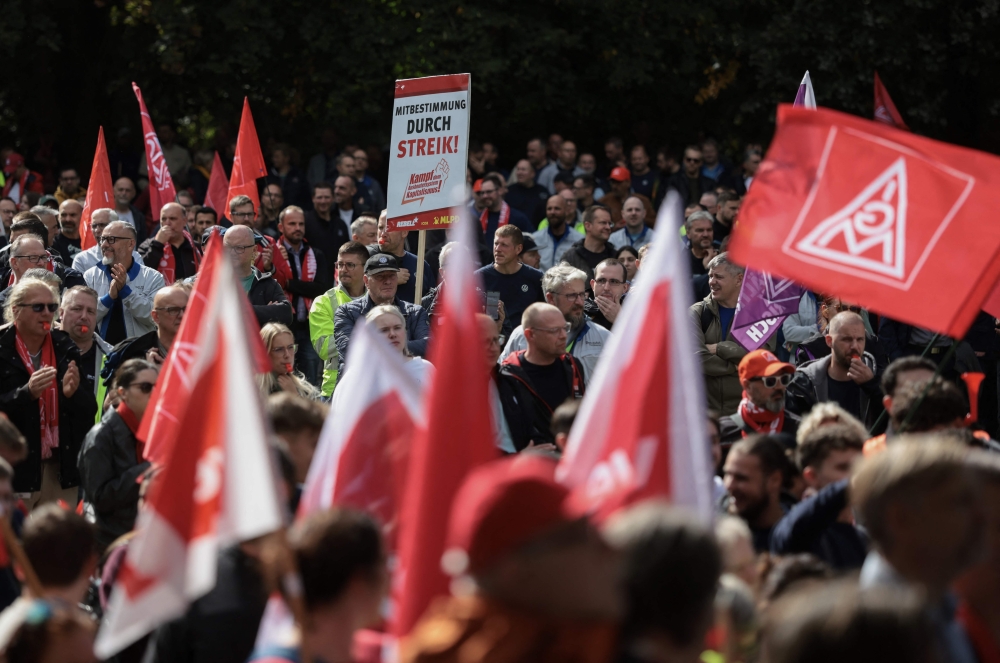 Workers wave flags of the industrial union IG Metall as they protest against job cuts in front of the commercial cars plant of German car maker Volkswagen (VW) on September 21, 2026 in Hanover, central Germany. (Photo by Ronny Hartmann / AFP)