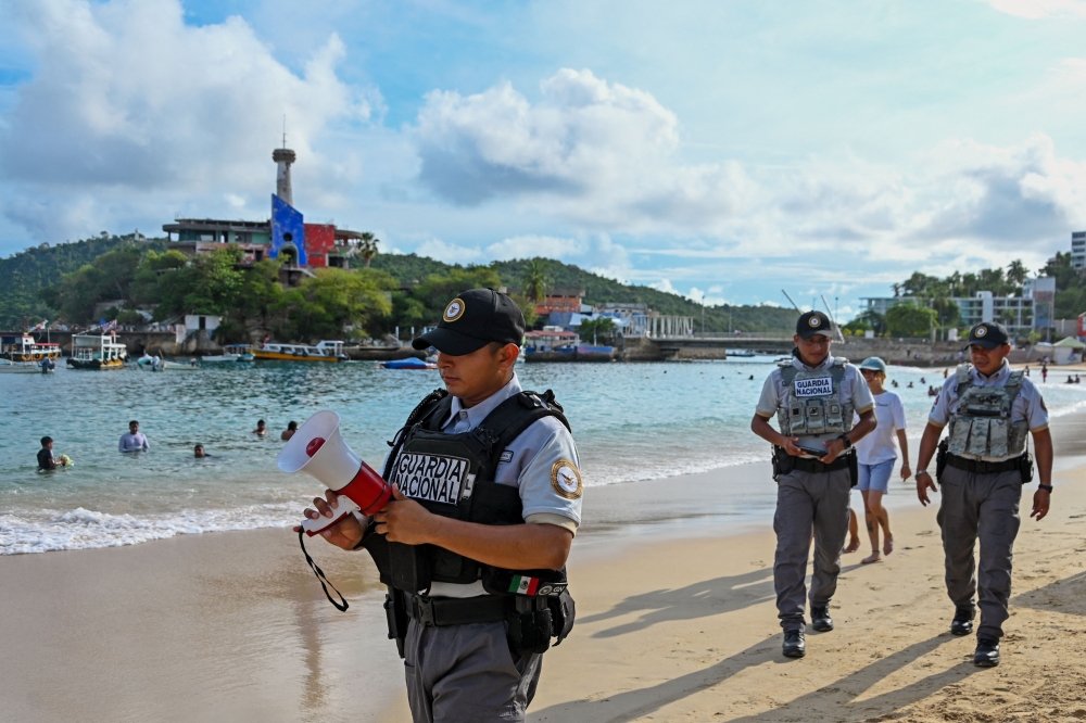 A member of the Mexican National Guard makes an announcement to residents and visitors about the approach of Hurricane Polo along a beach in Acapulco, Guerrero state, Mexico, on September 21, 2026.  (Photo by Francisco Robles / AFP)
