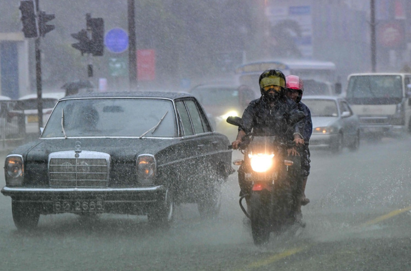 File photo showing commuters driving down a flooded street in Colombo. AFP file photo.