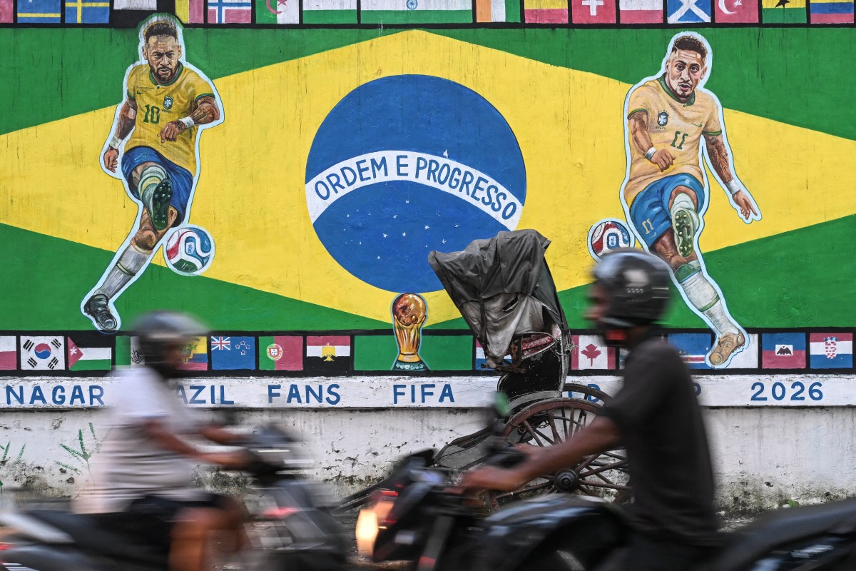 Motorcyclists ride past a graffiti featuring Brazilian football player Neymar (L) and Raphinha ahead of a FIFA international friendly football match between India and Brazil in Kolkata on September 29, 2026. (Photo by Dibyangshu Sarkar / AFP)

