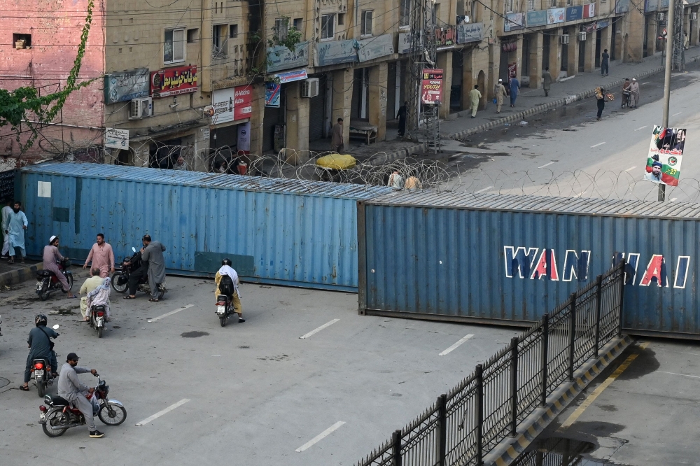 Commuters gather at a road blocked with shipping containers amid ongoing protests by the opposition Pakistan Tehreek-e-Insaf (PTI) party demanding the release of jailed former prime minister Imran Khan in Peshawar on October 11, 2026. (Photo by Abdul Majeed / AFP)