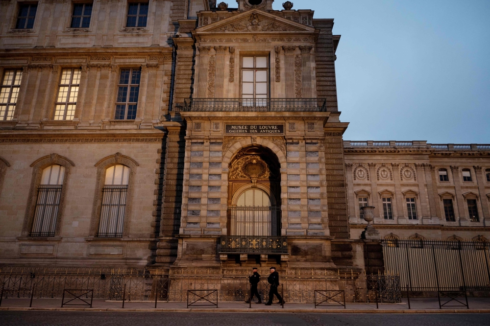 (Files) Police officers walk next to posts newly installed on the sidewalk along the Louvre Museum, on Quai Francois Mitterrand, in Paris on December 12, 2025. (Photo by Anna Kurth / AFP)
