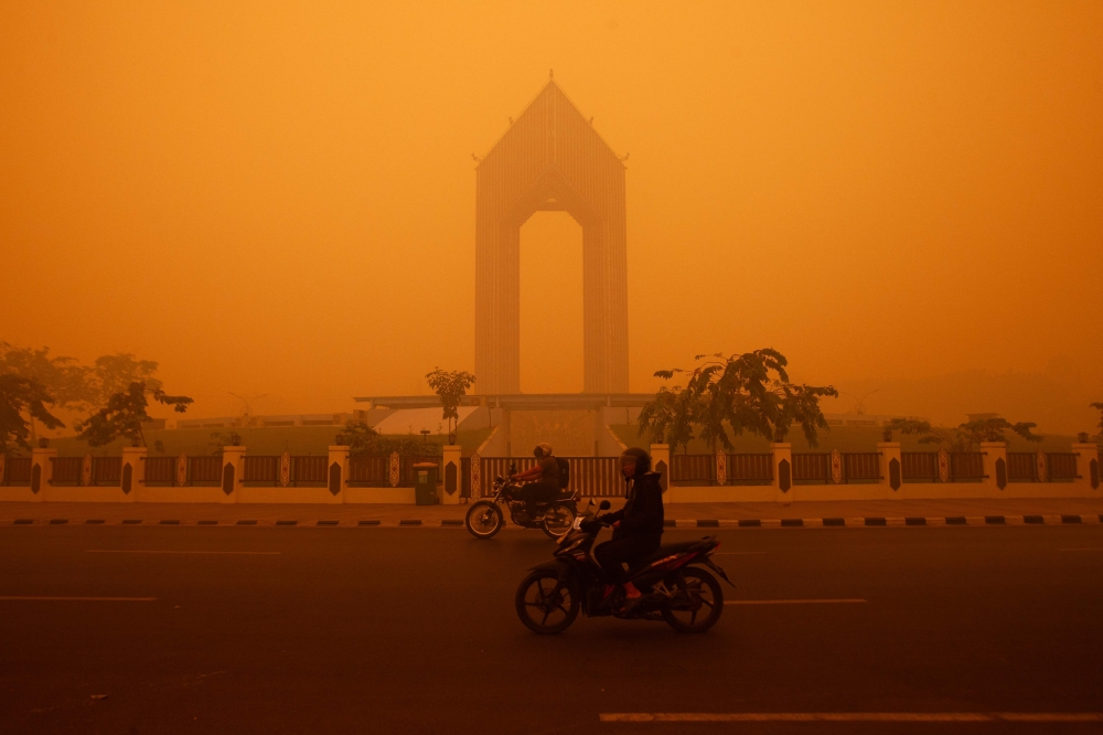 Motorcyclists ride in the morning in Palangkaraya, Central Kalimantan on October 14, 2026, amid thick haze from forest and land fires in the region. (Photo by Reina / AFP)