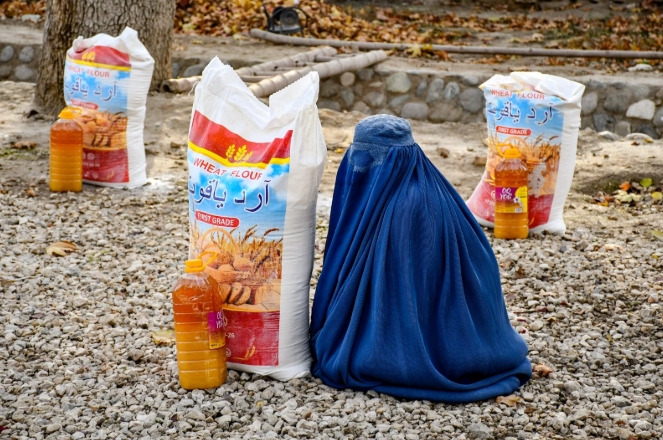 An Afghan burqa-clad woman sits next to food aid distributed by a local charity foundation in Mazar-i-Sharif. (AFP)