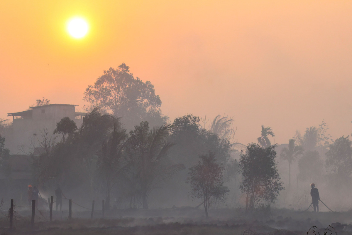 Firefighters and residents use hoses to extinguish spreading wildfires amid dense smoke and a hazy sunset in Banjarbaru, South Kalimantan province, on October 21, 2026. (Photo by MUDA SAGALA / AFP)