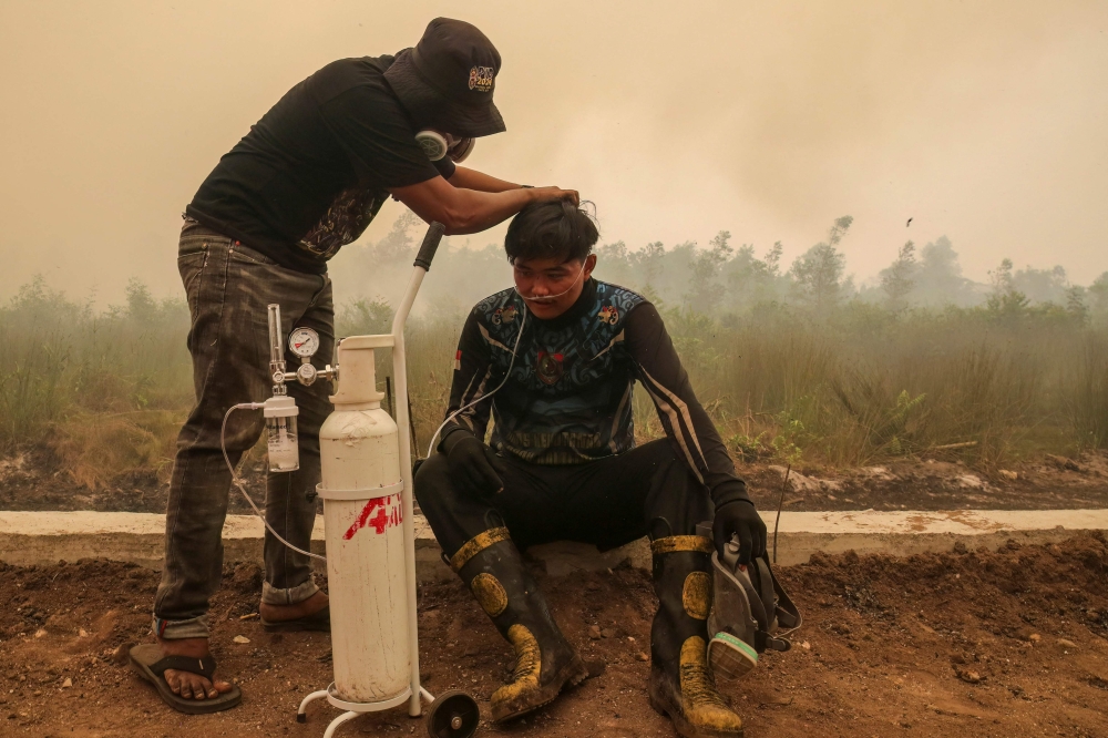 This picture taken on October 22, 2026 shows a volunteer from the Central Kalimantan Forest and Land Fire Smoke Response Coalition (RAKAT) providing mobile oxygen relief to a firefighter while battling forest and land fires in Palangkaraya, Central Kalimantan. (Photo by REINA / AFP)